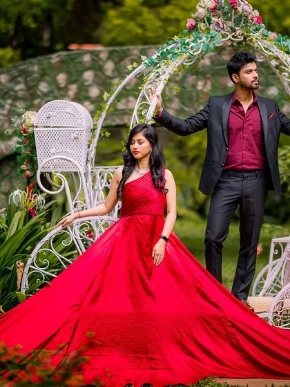 A modern fairy tale scene. The couple poses with the Cinderella carriage, and the long train of the red gown creates a dramatic, carpet-like effect on the ground.