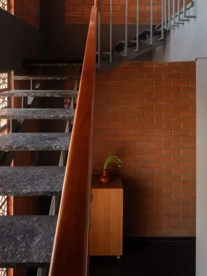 The staircase in the Madhura house is a study in contrasts, with cool granite steps, a simple metal railing, and warm terracotta jali screens that filter light.