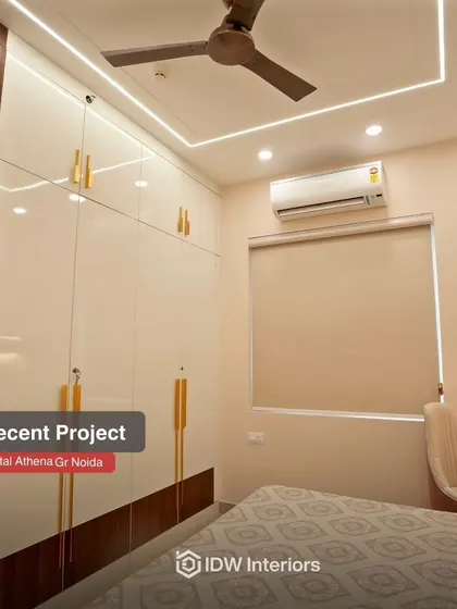 This bedroom design focuses on maximizing storage with sleek, glossy white and wood wardrobes featuring stylish gold handles.
