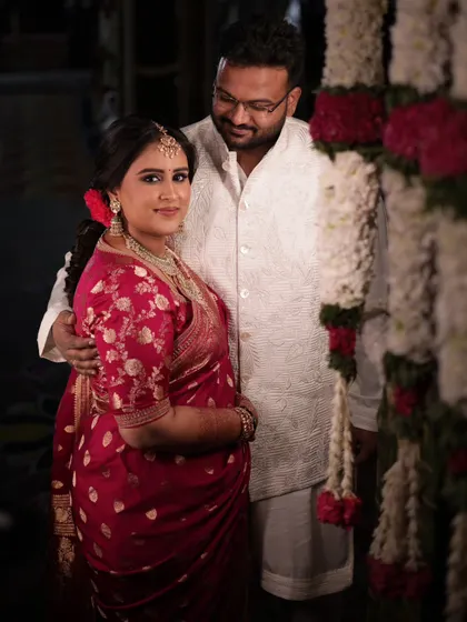 A lovely portrait of a couple during their housewarming ceremony. The decor features traditional floral garlands made of jasmine and roses, creating a warm and festive backdrop.