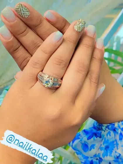 A soft baby blue ombre on natural nails, with accent nails featuring a textured gold geometric pattern.