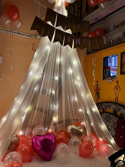 Another angle of the romantic canopy decoration. The warm fairy lights create a magical glow, while the mix of regular and heart-shaped foil balloons on the bed adds to the celebratory feel.