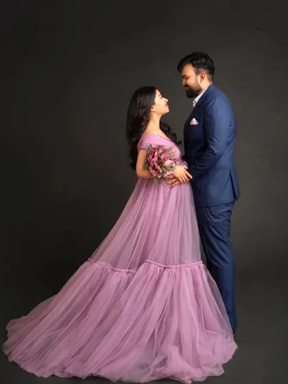 A romantic studio portrait of an expecting couple. The partner's formal suit complements the elegance of the lavender maternity gown, creating a timeless and classic image.