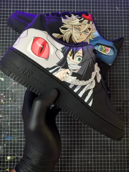 A Demon Slayer face-off between the Serpent Hashira, Obanai Iguro, and the formidable Upper Moon Two, Doma. The contrasting characters make for a dynamic design on these black AF1s.