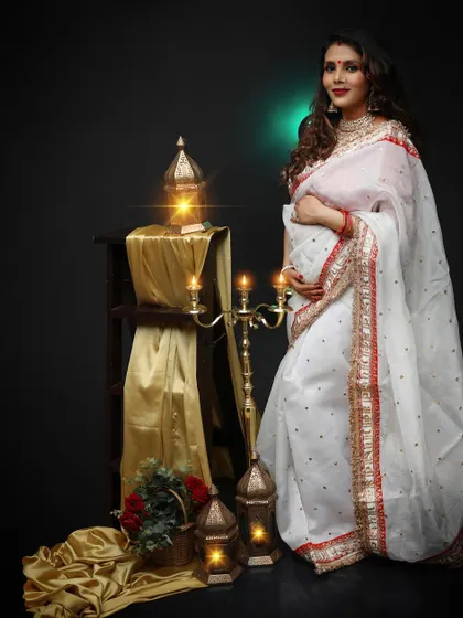 An eye-catching solo portrait of a mom-to-be in a beautiful white and red saree. She looks serene and graceful against the dark, traditionally styled set.