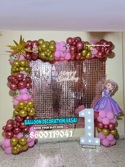 A royal first birthday party with a Princess Sofia theme. This decoration features a rose gold shimmer wall, a pink and gold balloon frame, and a Sofia the First cutout next to the marquee number.