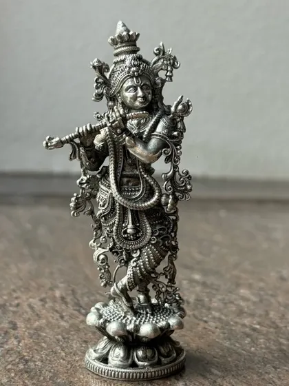 An intricately designed silver murti of Lord Krishna playing the flute. The oxidized finish enhances the detailed carvings on his attire and ornaments, giving it a timeless, antique look.