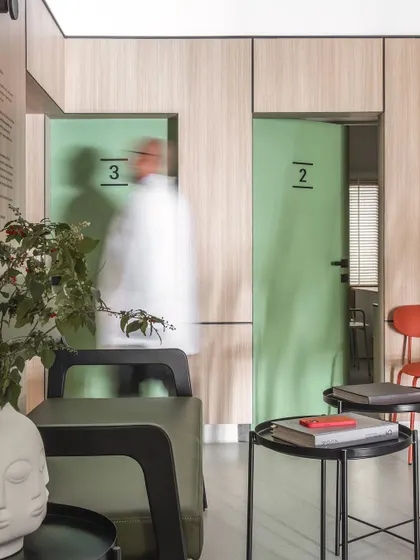 The use of a soft green for the doors adds a subtle touch of color that complements the natural oak panels. This color is associated with healing and tranquility, reinforcing the clinic's purpose.
