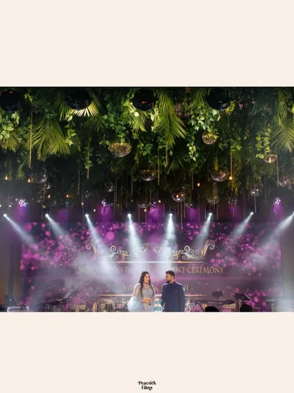 A wide shot of the engagement stage, with dramatic lighting and lush green decor creating a stunning backdrop for the couple.