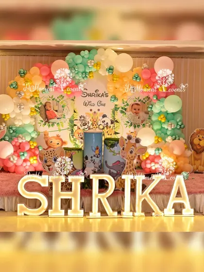 The full view of a pastel jungle-themed first birthday stage, complete with marquee letters and a variety of friendly animal props.