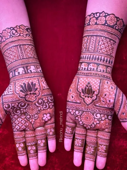 A breathtakingly intricate bridal design featuring a central lotus on each palm. The hands and arms are covered in a dense tapestry of elephants, florals, and geometric jaali patterns.