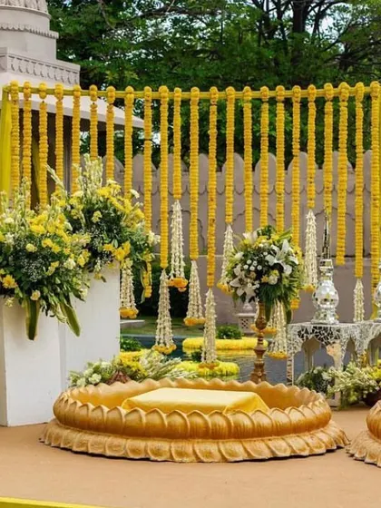 A luxurious Haldi setup with a marigold wall and elegant seating. The large floral arrangements and traditional lamps add a touch of opulence to the ceremony.