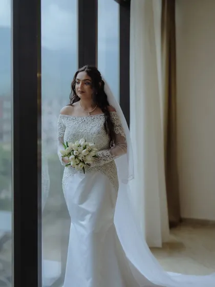 A full-length portrait of a Christian bride in her beautiful mermaid-style gown and long veil, looking out a window in a moment of quiet anticipation.