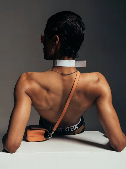 A full back view for a Calvin Klein accessories campaign. The pose and lighting are designed to draw attention to the bag and the defined musculature of the model.