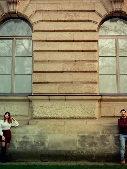 A minimalist and artistic shot of a couple posed against a large stone building. The distance between them creates a feeling of quiet connection and modern romance.
