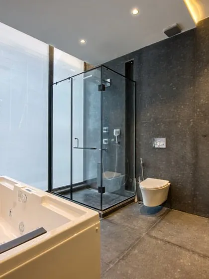 This bathroom combines a jacuzzi tub and a glass-enclosed shower. The large window allows for natural light, while the dark stone tiles create a grounded, earthy feel.