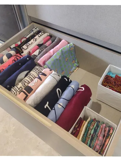 A drawer showing file-folded t-shirts and other tops, with smaller items contained in fabric boxes.