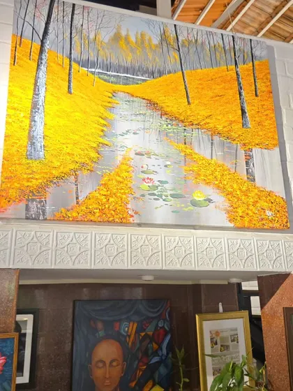 This large landscape painting of a river flowing through a forest with bright yellow leaves makes a stunning statement piece. It is displayed here in our gallery, showcasing how art can transform a space.
