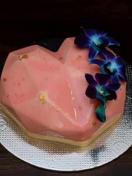 This geometric heart mousse cake has a beautiful pink mirror glaze finish. It's decorated simply with a few deep blue orchids, creating a striking contrast of colors and shapes.