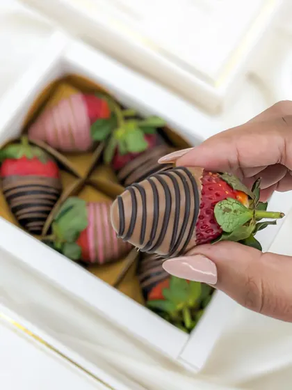 A close-up of a hand-picked, perfectly drizzled chocolate-coated strawberry, showcasing the quality and freshness.