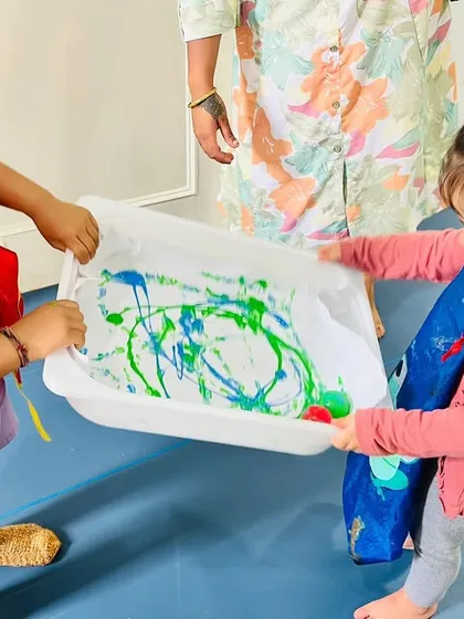 Another pair of young artists fully engaged in the marble painting process. They are learning to negotiate movement and share control of the tray, building important social-emotional skills.