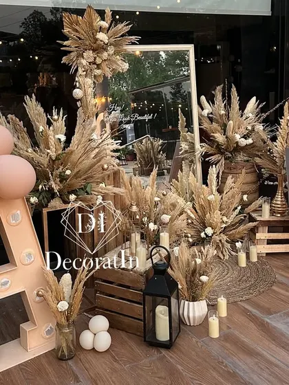 A rustic and chic photo corner for a 40th birthday. This setup includes a large marquee initial, a mirror for selfies, and is heavily decorated with dried pampas grass, wooden crates, and lanterns for a warm, bohemian feel.