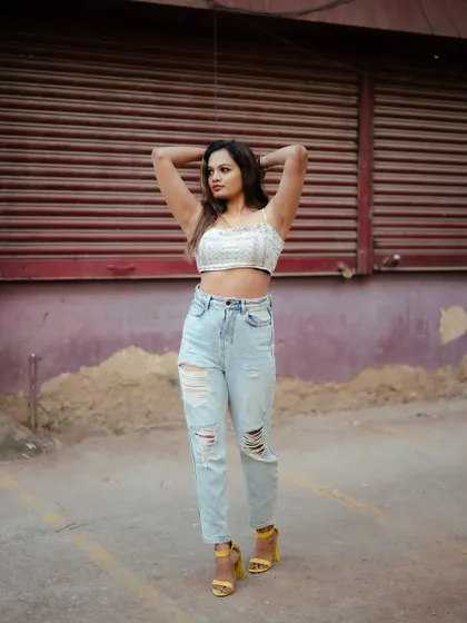 A full-length street style shot. The model's casual outfit and confident pose against the urban backdrop create a relatable and fashionable portrait.