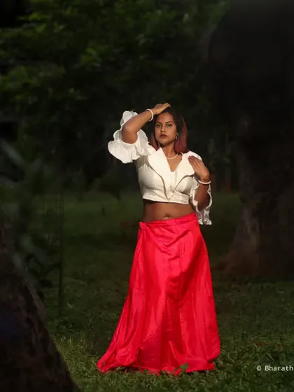 A full-length shot in a wooded area, capturing a dramatic pose. The lighting creates a moody, almost cinematic feel.