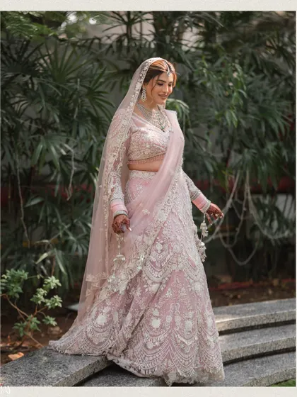 A full-length portrait of the Sikh bride, her pastel pink lehenga looking stunning against the green foliage.
