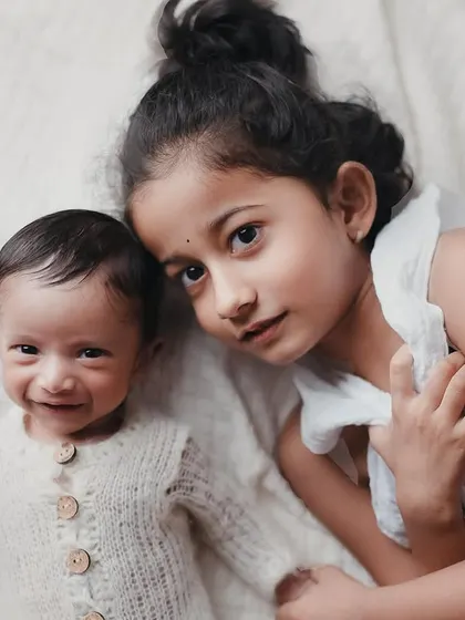 A close-up portrait of an older sister and her smiling newborn brother. This image is filled with so much tenderness and love.