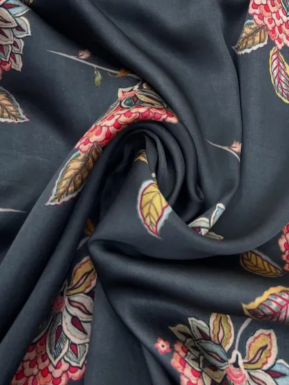 This printed modal fabric features a traditional floral design on a dark grey base. Its soft and glossy texture makes it a versatile choice for any wardrobe.