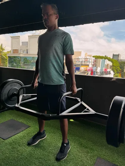 A client holds a heavy trap bar at the top of a deadlift, demonstrating the strength he has built through our programs.