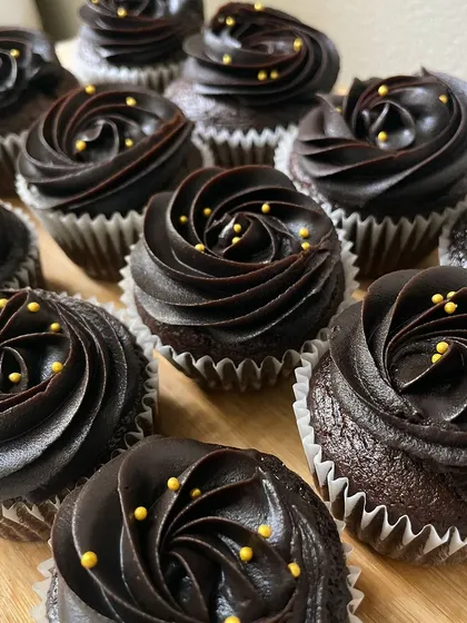 A close-up of our decadent chocolate cupcakes. The perfectly piped frosting and gold bead sprinkles add a touch of luxury to these popular party treats.