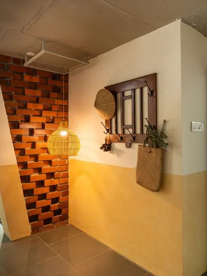 A view down the main corridor of "Aamra," showing the inclined wall and the play of light and shadow. The yellow oxide finish on the lower half of the wall adds warmth to the space.