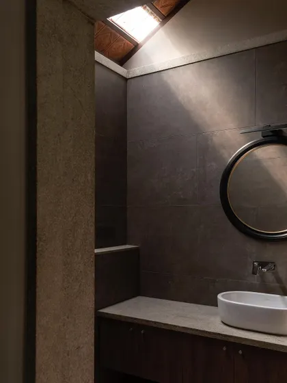 Another bathroom view, where a skylight casts a single ray of light across the dark stone tiles. The design creates a moody, atmospheric space, enhanced by the simple, elegant fixtures.