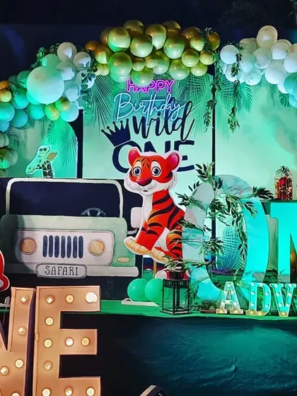 This outdoor jungle safari theme creates an adventurous vibe. The decor includes a prop jeep, friendly lion and tiger cutouts, and large marquee letters, all set against a backdrop of lush greenery.