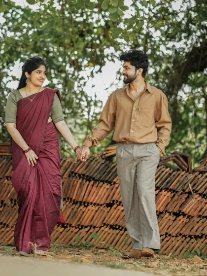 A pre-wedding photo with a rustic, countryside feel, as the couple walks hand-in-hand past a stack of traditional clay roof tiles.