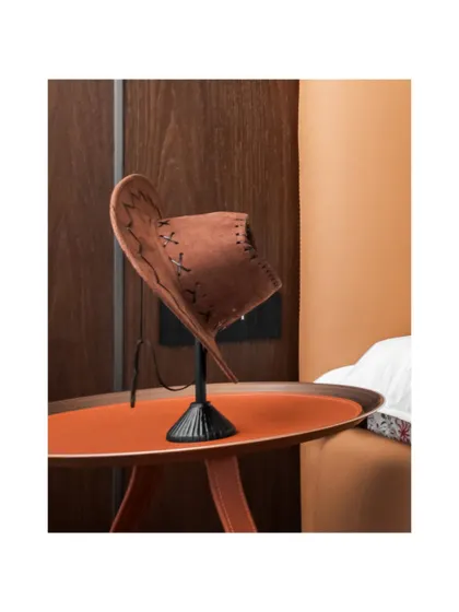 A close-up of a quirky styling detail: a suede hat resting on a stand on a bright orange side table. This shows how we inject personality and youthful energy into a sophisticated space.
