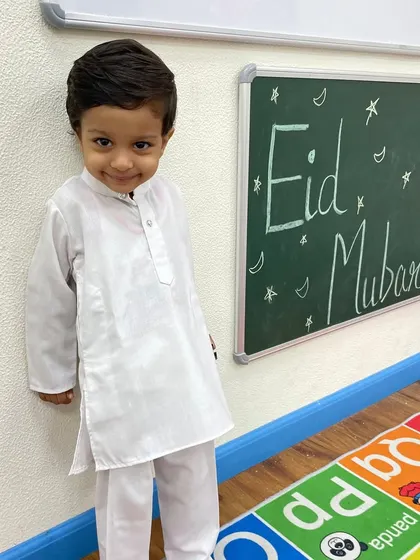 A little boy in a crisp white kurta stands proudly next to the 'Eid Mubarak' board. Our celebrations are designed to make every child feel special and included.