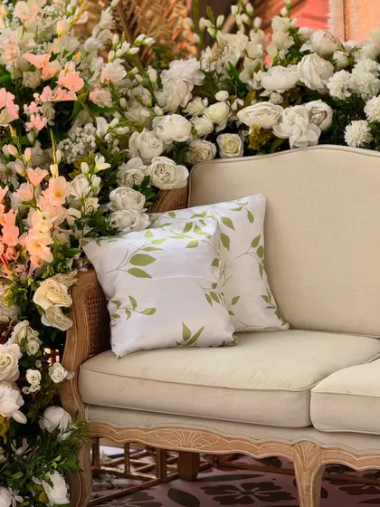 A close-up of a classic caned sofa, nestled in a corner of lush white and pink flowers. This demonstrates our belief that seating should be both comfortable and beautiful.