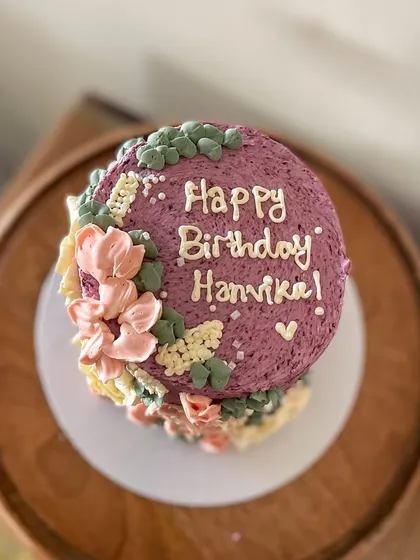This tall barrel cake is a great example of my floral buttercream work. The textured purple frosting is adorned with hand-piped flowers in pastel pinks and yellows, creating a beautiful garden effect.