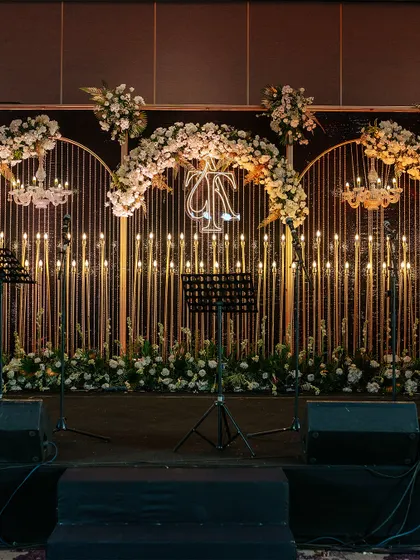 For a modern and chic Sangeet or reception, we designed this stunning stage featuring a wall of warm candle lights, elegant floral arches, and a personalized neon monogram for the couple.