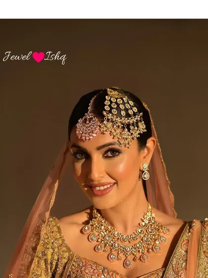 A smiling bride showcasing her unique headpiece, a combination of a pink-stone tikka and a polki passa. This is how we customize pieces to create a signature style.