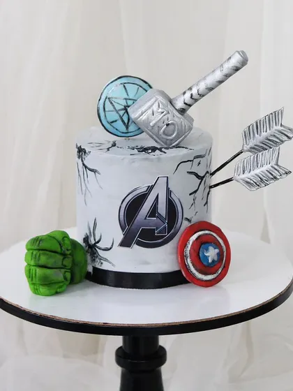 Assemble for the best birthday ever with this Avengers-themed cake. It features iconic symbols like Captain America's shield, Thor's hammer, and Hulk's fist, all meticulously crafted from fondant.