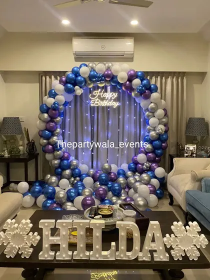 A full balloon ring in blue, purple, and silver, creating a dramatic and beautiful backdrop in a living room.