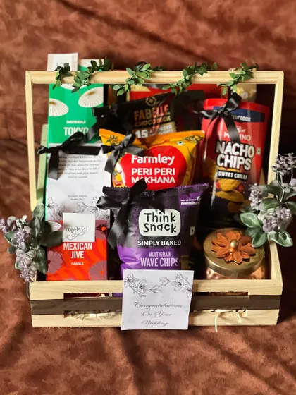 An open view of a wooden crate engagement hamper. It's packed with a selection of savory snacks like peri peri makhana, multigrain waves, and nacho chips, perfect for a couple to share.
