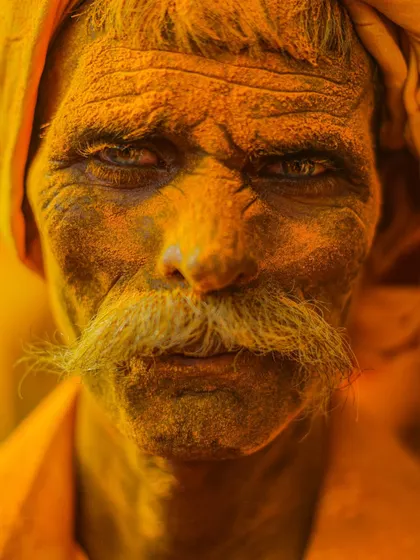 An intense, close-up portrait of a man at the Shri Vitthal Birdev Yatra in Pattan Kodoli. His face, covered in yellow turmeric powder, and his piercing gaze make for an incredibly powerful image.