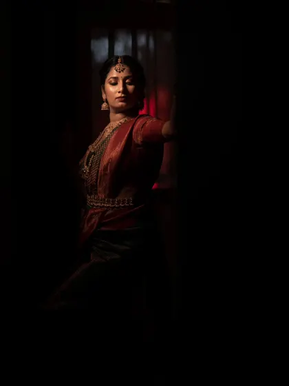 A low-key portrait where the bride emerges from the shadows. The deep blacks make the red of her saree even more vibrant, creating a mysterious and captivating image.