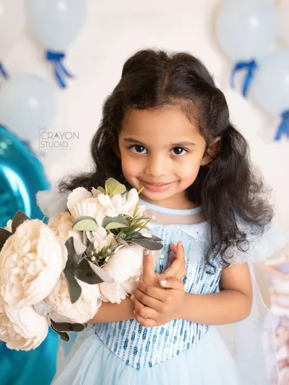 The birthday princess holds a bouquet of flowers, her gentle smile lighting up the studio.