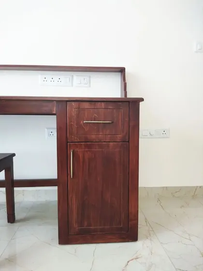 A minimalist home office setup featuring a sleek wooden desk, matching chair, and a slim storage cabinet. The natural light from the window creates a bright and productive workspace.